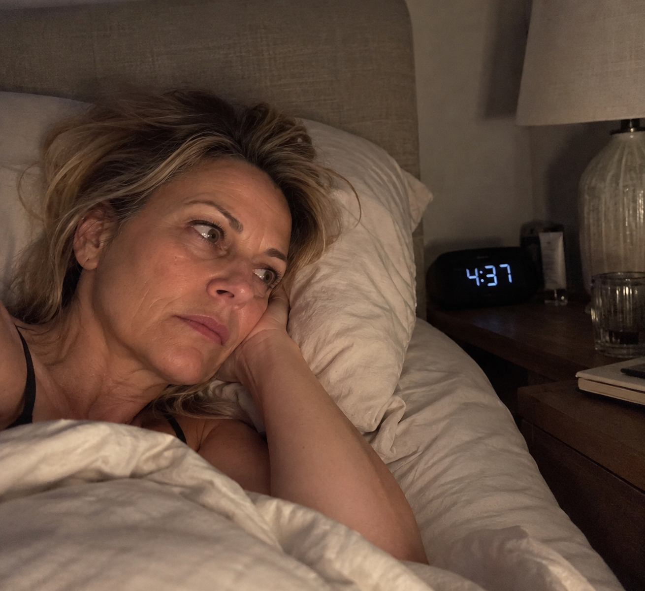 Frau liegt nachts wach im Bett, auf dem Wecker steht 04:37